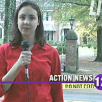 TV reporter standing in front of crime scene tape blocking the entrance to a mansion