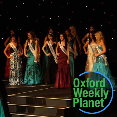 Contestants onstage at a beauty pageant with the Oxford Weekly Planet logo in the foreground