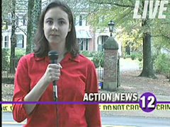 TV reporter standing in front of crime scene tape blocking the entrance to a mansion