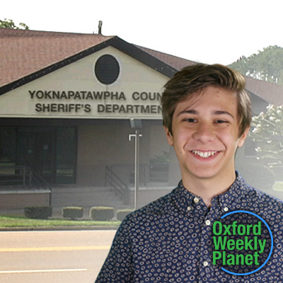 Smiling teen boy with medium brown hair with the sheriff's department in the background and the Oxford Weekly Planet logo in the foreground