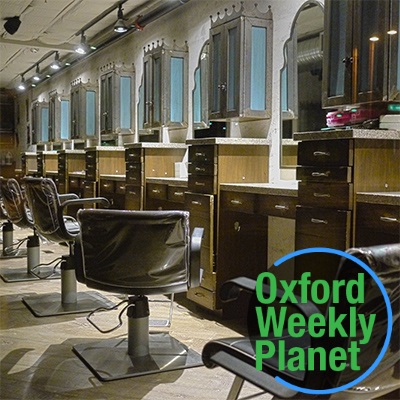 A row of stylist chairs in front of mirrors in a hair salon with the Oxford Weekly Planet logo in the foreground