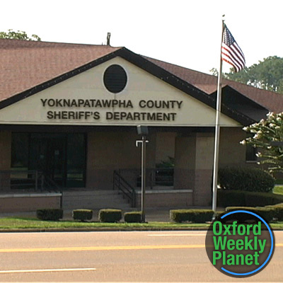 Exterior of the Yoknapatawpha County Sheriff's Department with the Oxford Weekly Planet logo in the foreground