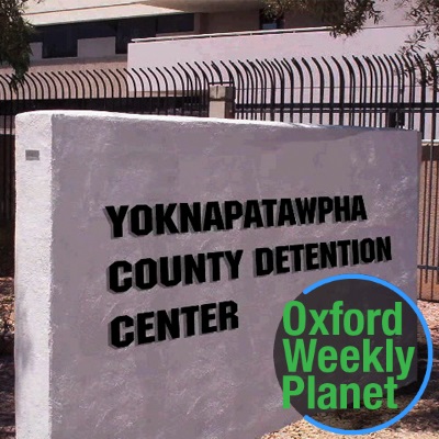 Exterior of the Yoknapatawpha County Detention Center with the Oxford Weekly Planet logo in the foreground