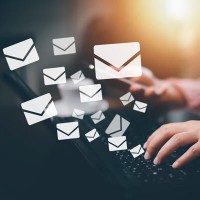 Woman typing on laptop with email icons in the foreground