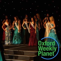 Contestants onstage at a beauty pageant with the Oxford Weekly Planet logo in the foreground
