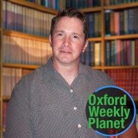 Serious man with short brown hair in a library with the Oxford Weekly Planet logo in the foreground