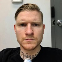 Serious-looking young man with short hair, facial hair, and tattoos