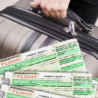 Hand holding a suitcase with airline tickets in the foreground