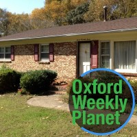 Front entrance of a ranch-style house with the Oxford Weekly Planet logo in the foreground