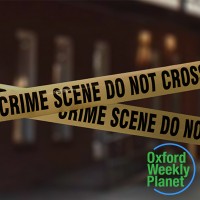 Crime scene tape in front of a building with the Oxford Weekly Planet logo in the foreground