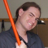 Smiling brown-haired man wearing coveralls and holding a broom