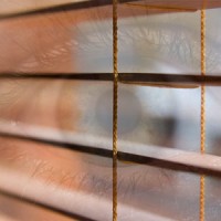 Close-up of an eye looking through window blinds