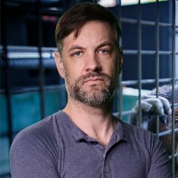 Man with dark hair and salt-and-pepper facial hair in front of an animal cage