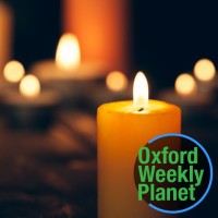 Candles burning on a dark background the Oxford Weekly Planet logo in the foreground