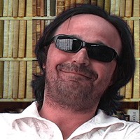 Smirking man with long dark hair and sunglasses