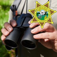Hands holding binoculars with the Yoknapatawpha County Sheriff's star in the foreground