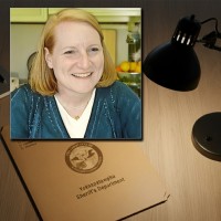 Smiling woman with a strawberry-blonde bob haircut in front of a manila folder stamped "Alibi"