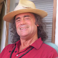 Man with long dark hair wearing a straw hat and red shirt