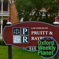 Sign for the Law Offices of Pruitt & Rayburn with the Oxford Weekly Planet logo in the foreground