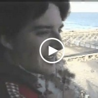 Video still of a man's face with the beach in the background and a video play button in the foreground