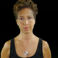 Unsmiling woman with short dark hair, wearing a black tank top