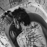 Black-and-white photo of a man lying face down in a bloody bathtub