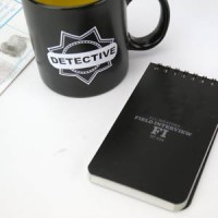 A detective coffee mug on a desk alongside a detective's notebook