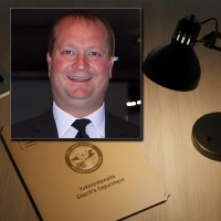 Smiling man with thinning hair in the foreground with a YCSD file folder on a desk in the background