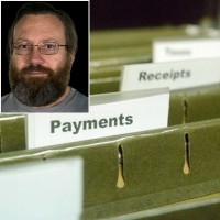 Hanging files with finance-related labels with an inset of a glasses-wearing man with brown hair, mustache and full beard in the foreground