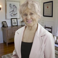 Woman with gray hair, wearing a light-colored jacket and black shirt