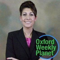 Smiling businesswoman with arms folded with the Oxford Weekly Planet logo in the foreground