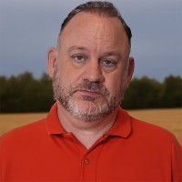 Unsmiling man with dark, thinning hair and salt-and-pepper facial hair