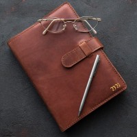 Monogrammed, brown leather notebook with silver pen and eyeglasses