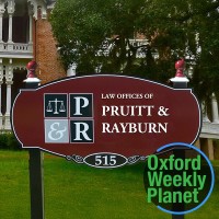 Sign for the Law Offices of Pruitt & Rayburn with the Oxford Weekly Planet logo in the foreground