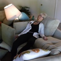 blonde woman dead on a sofa with the room disrupted around her