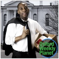 Man holding a file box and his suit jacket over his shoulder with the Oxford Weekly Planet logo in the foreground