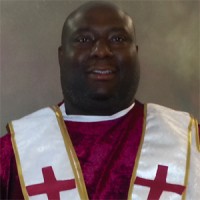 Large man in a red ministerial robe with a while stole trimmed in gold