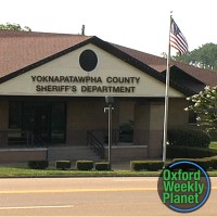 Exterior of the Yoknapatawpha County Sheriff's Department building with the Oxford Weekly Planet logo in the foreground