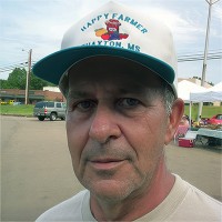 Man with gray hair and five o'clock shadow, wearing a trucker hat
