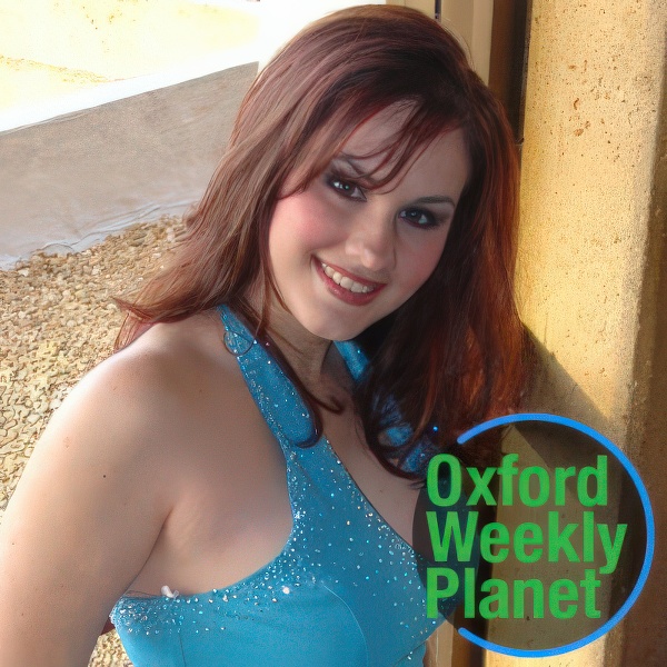 Long-haired woman in an evening gown with the Oxford Weekly Planet logo in the foreground