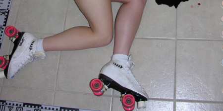 The legs of a woman lying on the floor wearing roller skates alongside the edge of a blood pool