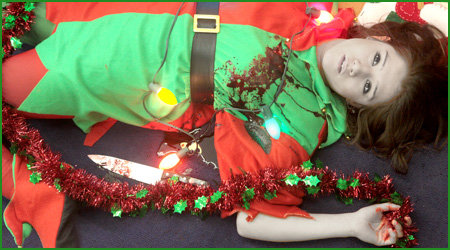 Young woman in a Christmas elf costume with a bloodstain on the left chest and a red-stained butcher knife on the floor beside her