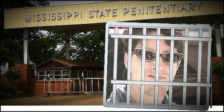 A man in sunglasses behind bars with the entrance to a penitentiary in the background