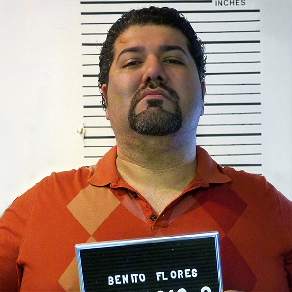 Man with dark hair and goatee in front of a police height chart