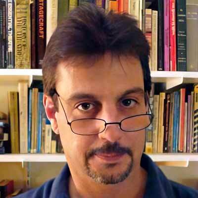 Man with dark hair and facial hair, looking over the top of his glasses