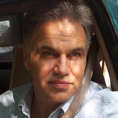 Unsmiling man with salt-and-pepper hair sitting in a vehicle driver's seat