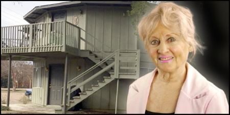 An older woman with blonde hair in front of an apartment building