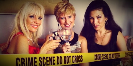 Three women in cocktail dresses holding wine glasses with crime scene tape in the foreground