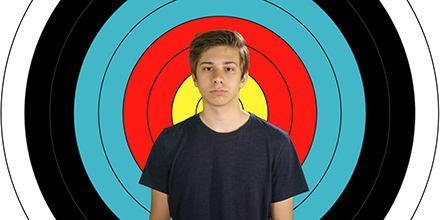 Glum teen boy standing in front of an archery target