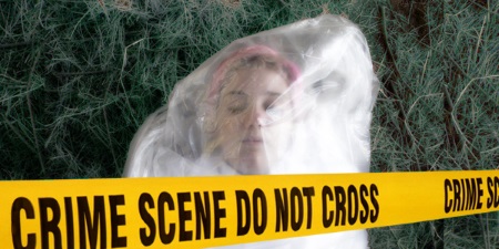 Pink-haired young woman wrapped in clear plastic lying on the grass with crime scene tape in the foreground